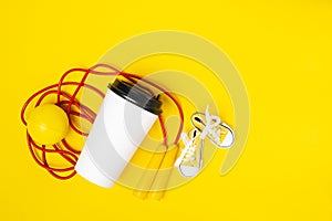 a jump rope, a yellow ball, a white paper cup and yellow sneakers on a yellow background. Active sports