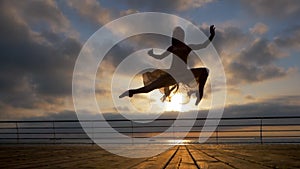 Jumping ballerina in beige dress and pointe on embankment above ocean or sea beach at sunrise.Beautiful blonde woman