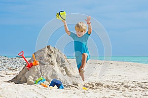 Jumping boy play with sand shovel bucket at the ocean beach