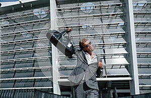 Jumping and celebrating success. Young businessman in grey formal wear is outdoors in the city