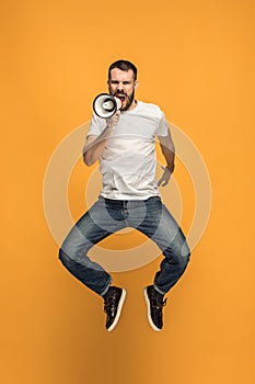 Jumping fan on orange background. The young man as soccer football fan with megaphone