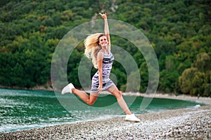 Jumping happy girl on sea coast on background of green forest