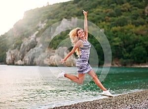 Jumping happy woman on sea coast on background of mountains