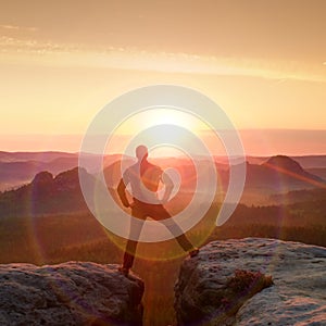 Jumping hiker in black celebrate triumph between two rocky peaks. Wonderful daybreak with sun above head..