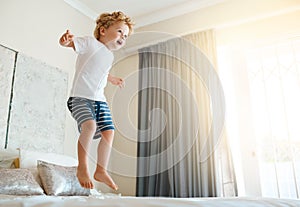 Jumping for joy. an adorable little boy jumping on the bed at home.