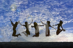 Girls jumping with Joy on the beach silhouetted against a cloudy sky