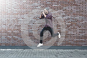 Jumping man with retro photo camera Fashion Travel Lifestyle outdoor while standing against brick wall background