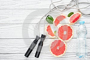 Jumping-rope, fresh grapefruits and bottle of water, on rustic white wooden table , top view, flat lay, fitness accessories.