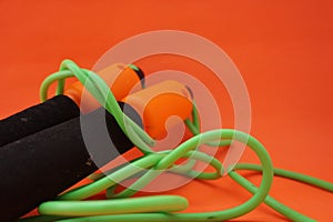 Jumping rope isolated on an orange background. Fitness and gym concept. Banners for websites, news. Green jump rope for exercise