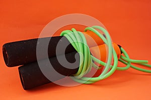 Jumping rope  on an orange background. Fitness and gym concept. Banners for websites, news. Green jump rope for exercise