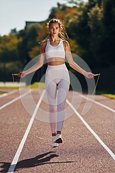 Jumping on the running track. Young woman in sportive clothes is exercising outdoors