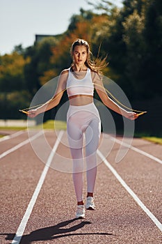 Jumping on the running track. Young woman in sportive clothes is exercising outdoors