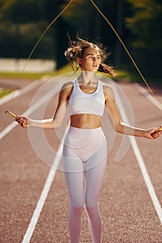 Jumping on the running track. Young woman in sportive clothes is exercising outdoors