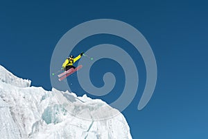 A jumping skier jumping from a glacier against a blue sky high in the mountains. Professional skiing