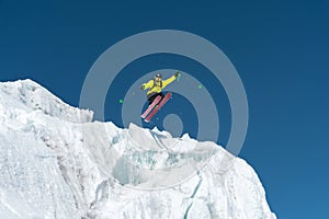 A jumping skier jumping from a glacier against a blue sky high in the mountains. Professional skiing