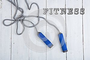 Jumping/skipping rope with blue handles on white wooden background with text fitness