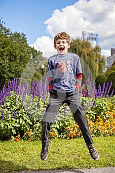 Jumping and smiling eight year old boy in city garden