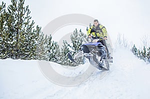 Jumping on a snowmobile on a background of winter forest. Bright snowmobile. Athlete on a snowmobile moving in the