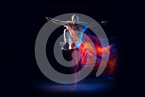 Jumping. Stylish man in sports white outfit dancing hip-hop, breakdance isolated on dark background in mixed neon light