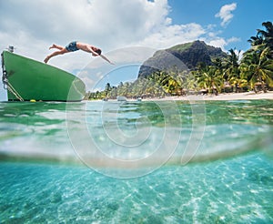 Jumping teenage boy from wooden boat snorkeling in clean turquoise lagoon on Le Morne palm trees beach with Le Morne Brabant mount