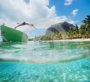 Jumping teenage boy from wooden boat snorkeling in clean turquoise lagoon on Le Morne palm trees beach with Le Morne Brabant mount