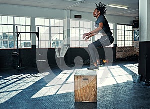 Jumping towards my fitness goals. a young man doing jumping exercises on a wooden block in a gym.