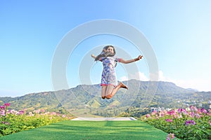 Jumping Young Asian woman feeling free with arms wide open at beautiful trees and mountains on blue sky