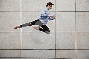 Jumping young buinessman in front of buildings, on the run in jump high