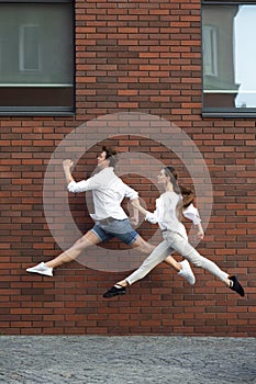 Jumping young couple in front of buildings, on the run in jump high