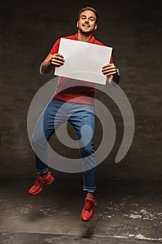 Jumping young man in jeans and red t shirt holding white sheet o