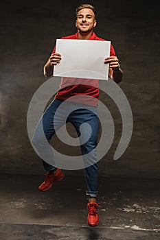 Jumping young man in jeans and red t shirt holding white sheet o