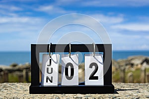 Jun 02 calendar date text on wooden frame with blurred background of ocean.
