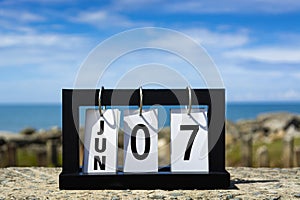 Jun 07 calendar date text on wooden frame with blurred background of ocean.