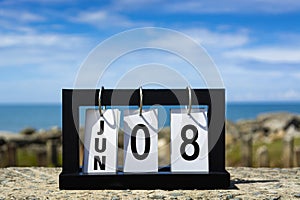 Jun 08 calendar date text on wooden frame with blurred background of ocean.