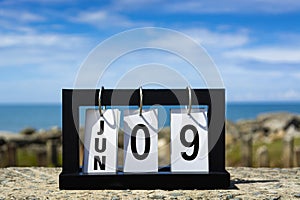 Jun 09 calendar date text on wooden frame with blurred background of ocean.