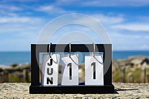 Jun 11 calendar date text on wooden frame with blurred background of ocean.