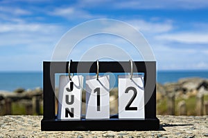 Jun 12 calendar date text on wooden frame with blurred background of ocean.