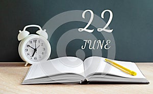 June 22. 22-th day of the month, calendar date.A white alarm clock, an open notebook with blank pages, and a yellow