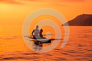 June 21, 2021. Antalya, Turkey. Woman with children paddle on stand up paddle board at quiet sea in evening. Woman and girl on Red