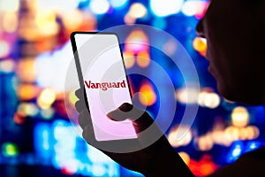 June 27, 2022, Brazil. In this photo illustration, a silhouetted woman holds a smartphone with the Vanguard Group logo displayed