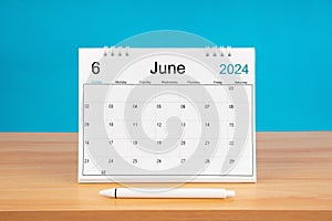 June monthly desk calendar for 2024 year and pen on wooden table with blue background