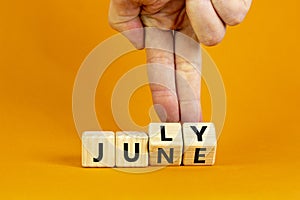 From june to july symbol. Businessman turns wooden cubes and changes the word `june` to `july`. Beautiful orange background, c