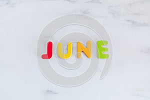 June word written with colorful letters on white marble stone background