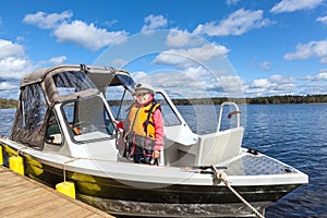 Jung child in captain's cap standing on wooden pier in moored motor boat