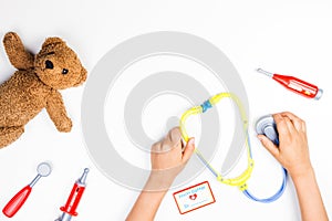 Kid hands with toy stethoscope, teddy bear and toy medicine tools on a white background. Top view. photo