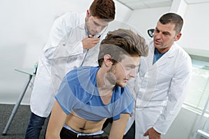 Junior doctor listening to young man`s back photo