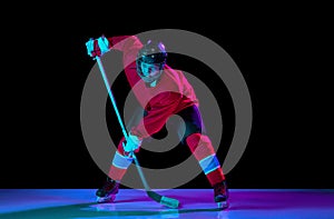 Junior ice hockey player in sports uniform and protective equipment in action over dark background in neon light. Sport