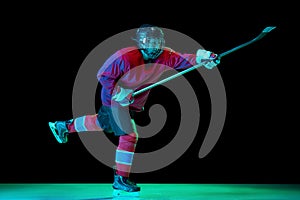 Junior ice hockey player in sports uniform and protective equipment in action over dark background in neon light. Sport