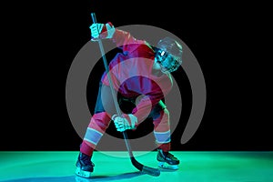 Junior ice hockey player in sports uniform and protective equipment in action over dark background in neon light. Sport