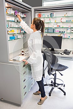 Junior pharmacist taking medicine from shelf